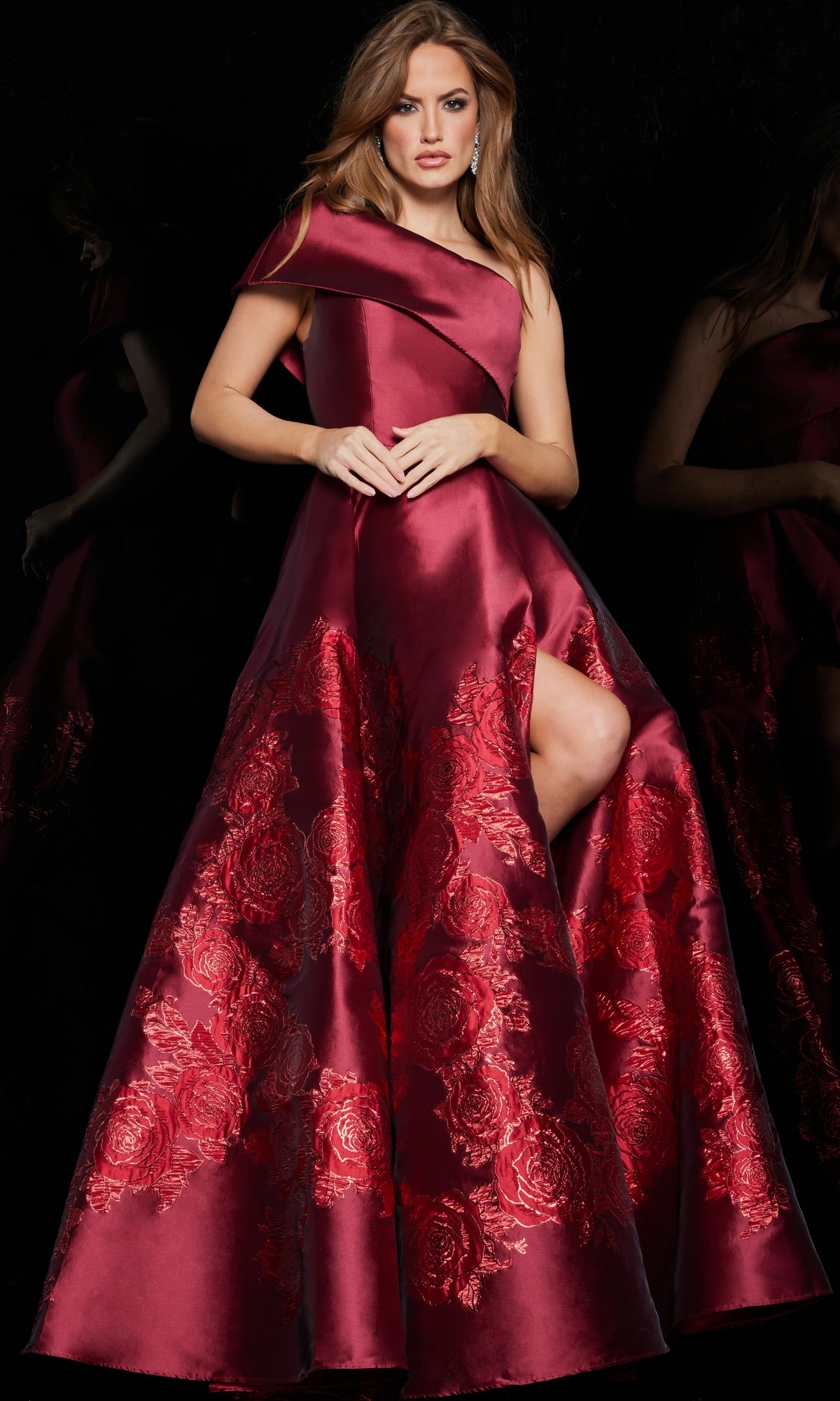 A woman poses against a black background in the Jovani Long Red One-Shoulder Prom Ball Gown 09610, featuring floral embroidery and a thigh-high slit.